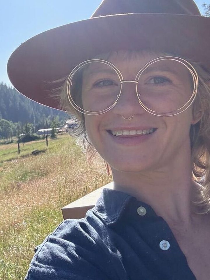 Sasha, smiling in a sunlit meadow with the forest behind her.